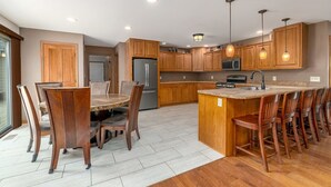 Une cuisine moderne avec des meubles en bois, un îlot central doté de tabourets de bar, une table à manger avec des chaises et des appareils électroménagers intégrés.