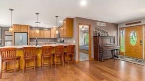 Une cuisine moderne avec des meubles en bois, un îlot central doté de tabourets de bar, un piano intégré et une grande porte en bois.