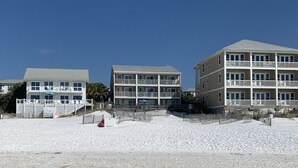 A beachfront hotel with multiple floors, outdoor seating, and a sandy beach in the foreground. - Remodeled 2020  Gulf front Private condo (Santa Rosa Beach)