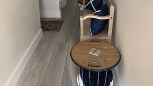 A narrow hallway with a wooden bench, a round table, and a bed in the background. - Remodeled 2020  Gulf front Private condo (Santa Rosa Beach)