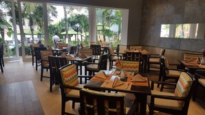 Ein Restaurant mit Holztischen und -stühlen, einige mit bunten Kissen.
