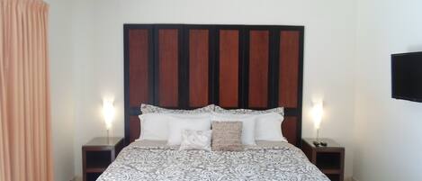 A bedroom with a large bed, a ceiling fan, and a TV mounted on the wall.