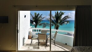 Ein Balkon mit Tisch und Stühlen, der Blick auf einen Strand mit Palmen und den Ozean freigibt.