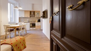 Une cuisine moderne avec des meubles en bois, un coin repas comprenant une table et des chaises, et une porte en bois foncé dotée d’une poignée en laiton.