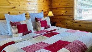 Un dormitorio de cabaña de madera con cama, almohadas y mesita de noche.
