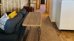 Ein Wohnzimmer mit einem dunkelgrauen Sofa, einem gewebten Couchtisch und Holzboden. Eine weiße Kühlmaschine ist rechts im Bild zu sehen.