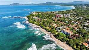 Una vista aerea di una cittadina costiera con spiaggia, edifici e imbarcazioni all'orizzonte.