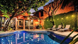 Una piscina con lettini, un'area relax coperta e una parete ricca di vegetazione.