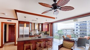 A modern kitchen with a central island, wooden bar stools, and a ceiling fan. - Relaxing 4th floor with Lap Pool View - Ocean Tower Beach Villa (Kapolei)