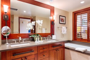 Une salle de bain dotée d’un grand miroir, de deux lavabos, d’un meuble-lavabo avec des tiroirs, d’une orchidée en pot et d’un porte-serviettes.