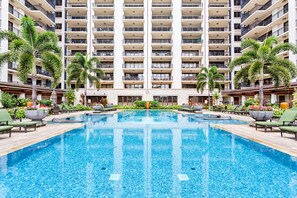Une grande piscine intérieure entourée de chaises longues et de palmiers, avec un immeuble de grande hauteur en arrière-plan.