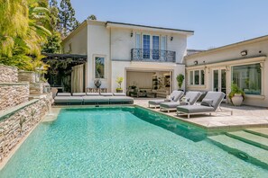 Ein modernes Haus mit Schwimmbad, Sitzgelegenheit im Freien und einem Balkon.