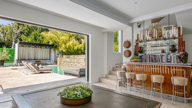 A modern kitchen with a bar area, a dining table with a centerpiece, and a view of the outdoor patio.