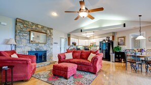 A spacious living room with a stone fireplace, a red sofa set, and a dining area with a chandelier. - Bella Regalo, Private 2BR, 2BA Mountain Escape, Upgraded with Panoramic Views (Pisgah Forest)