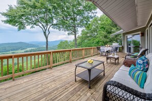 A wooden deck with outdoor furniture, a grill, and a scenic view of hills and trees.