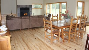 Un salon spacieux avec une cheminée, une grande table à manger en bois et des chaises, ainsi qu’un ensemble de canapés.