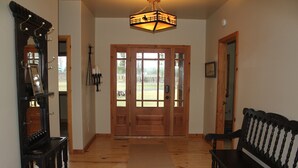 Un couloir au plancher de bois, avec un banc, un miroir et une porte dotée de panneaux de verre.