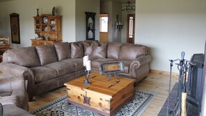 Un salon comprenant un canapé d’angle en cuir marron, une table basse en bois, un tapis à motifs, un meuble en bois et une cheminée.
