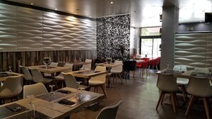 A modern restaurant interior with multiple dining tables and chairs, a decorative wall with a wave pattern, and a view of the outdoors through large windows. - Hotel de la Gare (Modane)