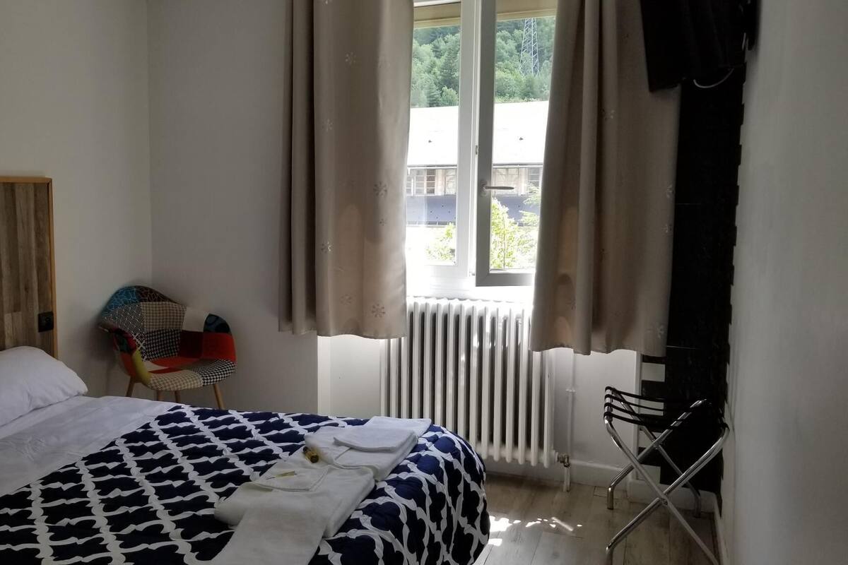 Une chambre à coucher avec un lit, une chaise, une fenêtre avec des rideaux et un radiateur.