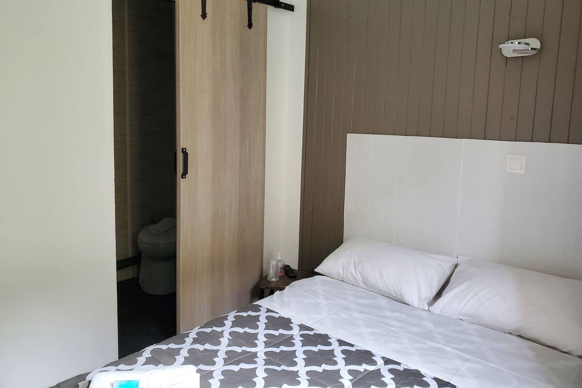 Une chambre à coucher avec un lit, une armoire en bois et une petite table sur laquelle se trouvent une bouteille et un téléphone.