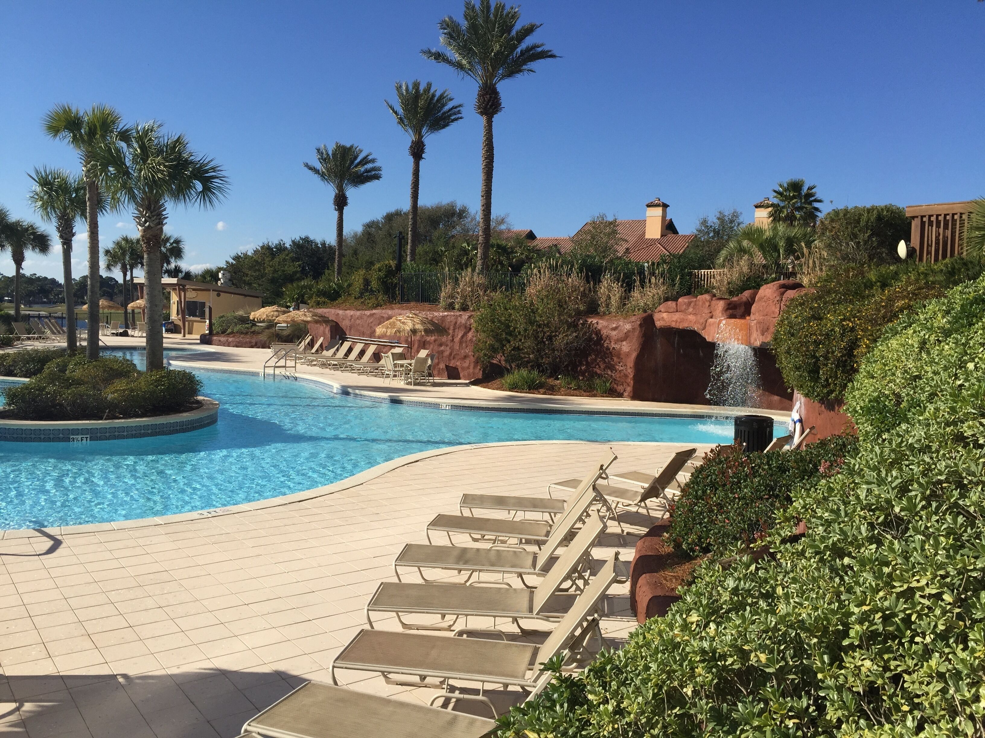 A resort pool with lounge chairs, palm trees, and a waterfall feature.