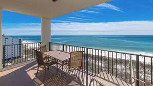 A balcony with a table and chairs overlooking a beach.