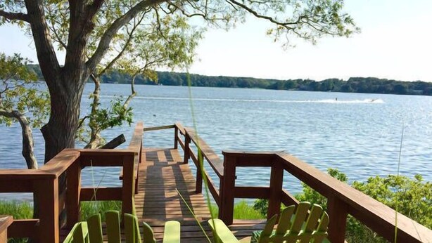 Eine Holzterrasse mit Stühlen mit Blick auf einen See.