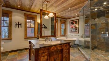 Une salle de bain avec des poutres en bois au plafond, un grand miroir, deux lavabos et une douche à parois de verre.