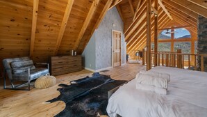 Une chambre avec un plafond en bois, un lit, une chaise, un tapis et une vue sur l’extérieur.