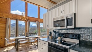 Une cuisine avec des armoires blanches, un four à micro-ondes en acier inoxydable et une cuisinière noire. Une fenêtre offre une vue sur les montagnes.