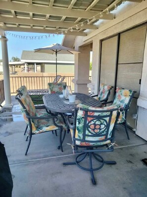 An outdoor patio with a round table and chairs, an umbrella, and a view of a building in the background. - Colorado River Mohave ValleyAZ-Private Bch & Lnch Ramp-Cabral Riverfront Oasis-2 (Mohave Valley)