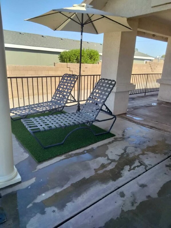 A covered outdoor seating area with two lounge chairs and a table, a green artificial turf, and a large umbrella. - Colorado River Mohave ValleyAZ-Private Bch & Lnch Ramp-Cabral Riverfront Oasis-2 (Mohave Valley)