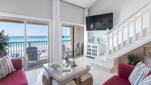 Un vaste espace de vie avec une table en verre, des canapés rouges et une vue sur la plage.