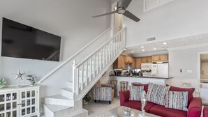 Un vaste salon comprenant un escalier, un canapé rouge, une table basse en verre et un téléviseur à écran plat fixé au mur.