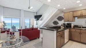 Un vaste espace de vie comprenant un canapé rouge, une table à manger en verre et une cuisine dotée de meubles en bois et d’un plan de travail noir.
