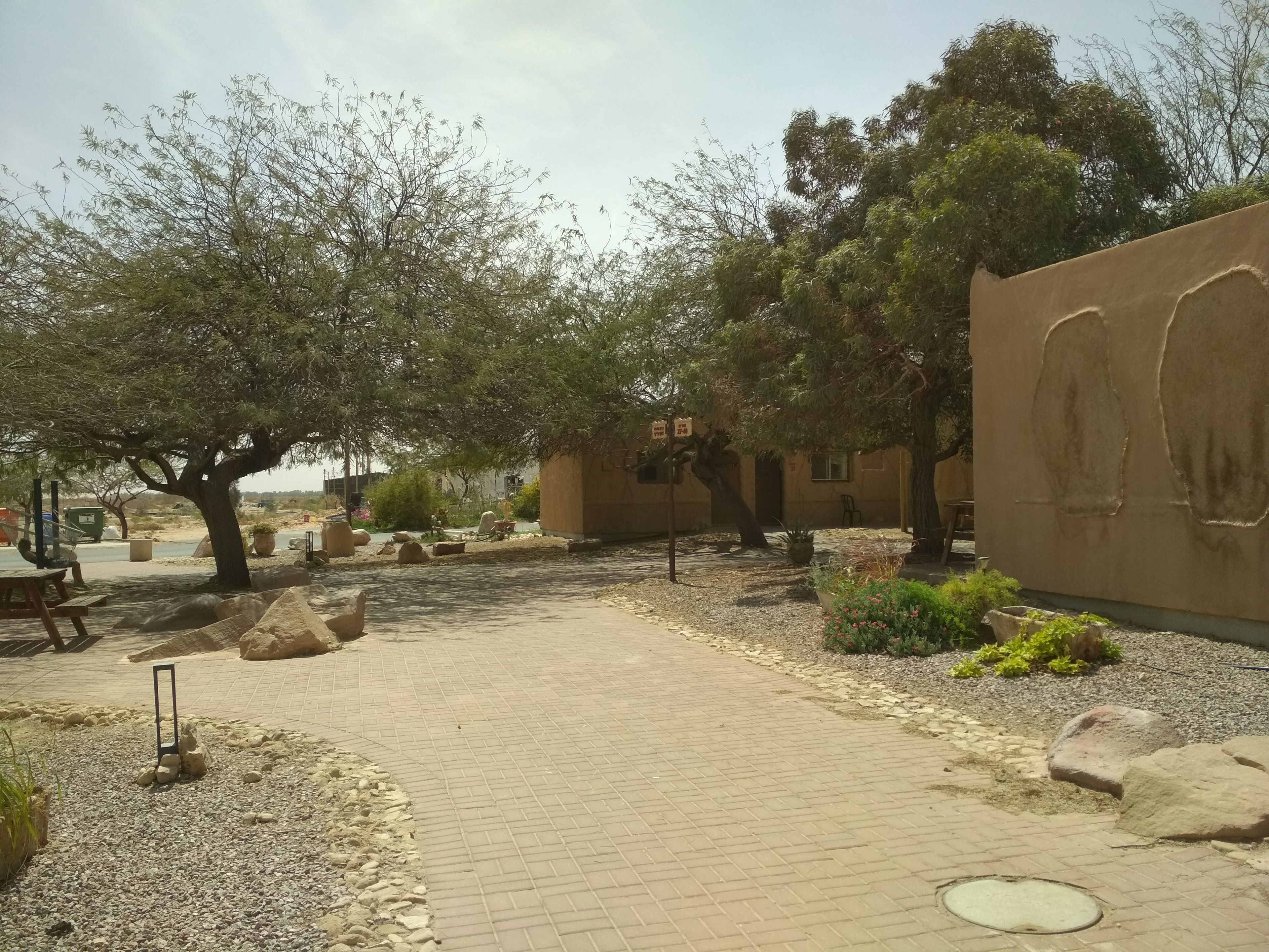 A paved pathway with a stone border, trees, and a wall with a relief sculpture.