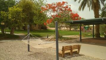 A hammock and wooden benches in a park area with a playground in the background.