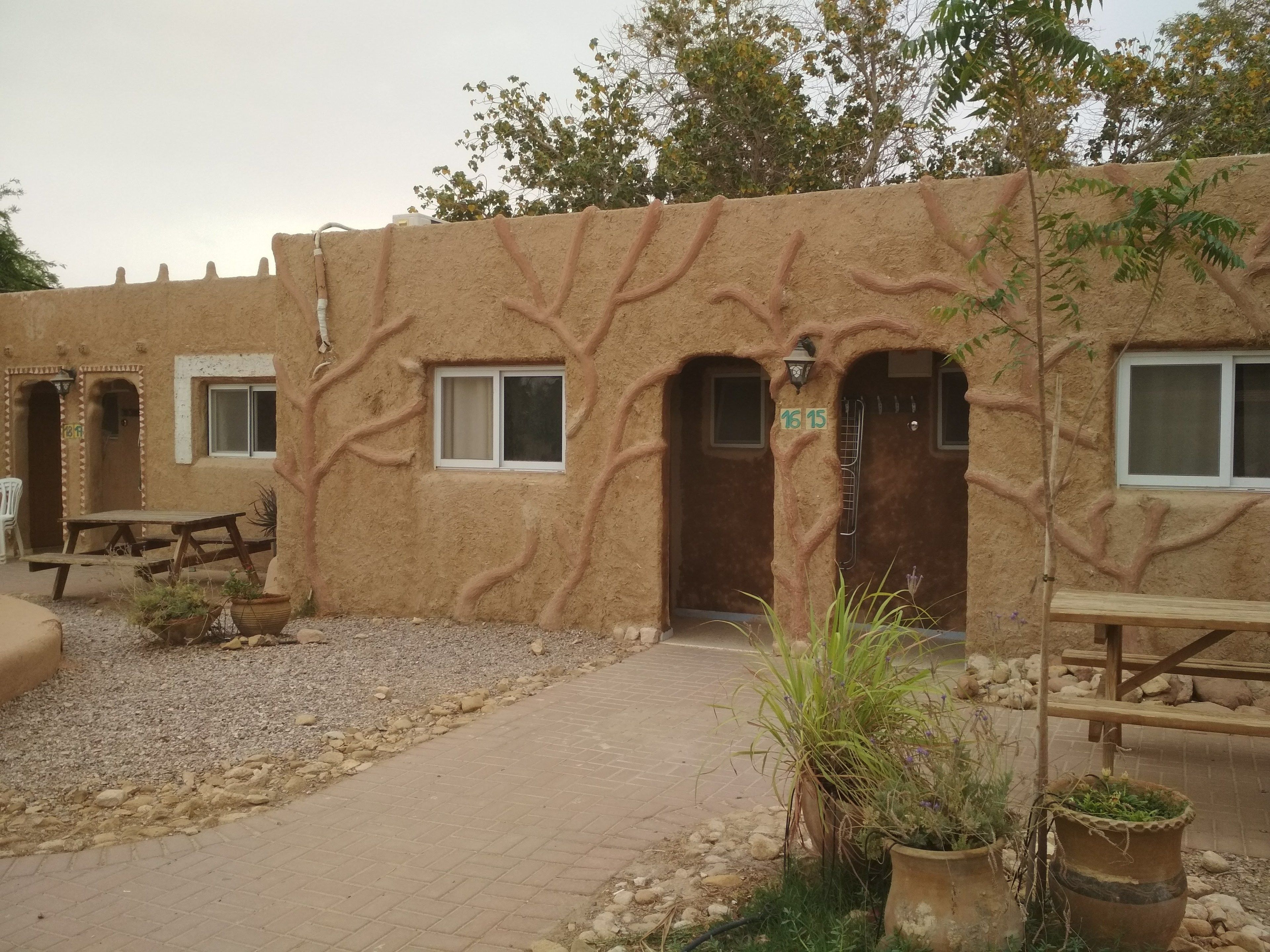 Un edificio rústico con fachada de piedra, varias ventanas y un área de acceso pavimentada con plantas en macetas.