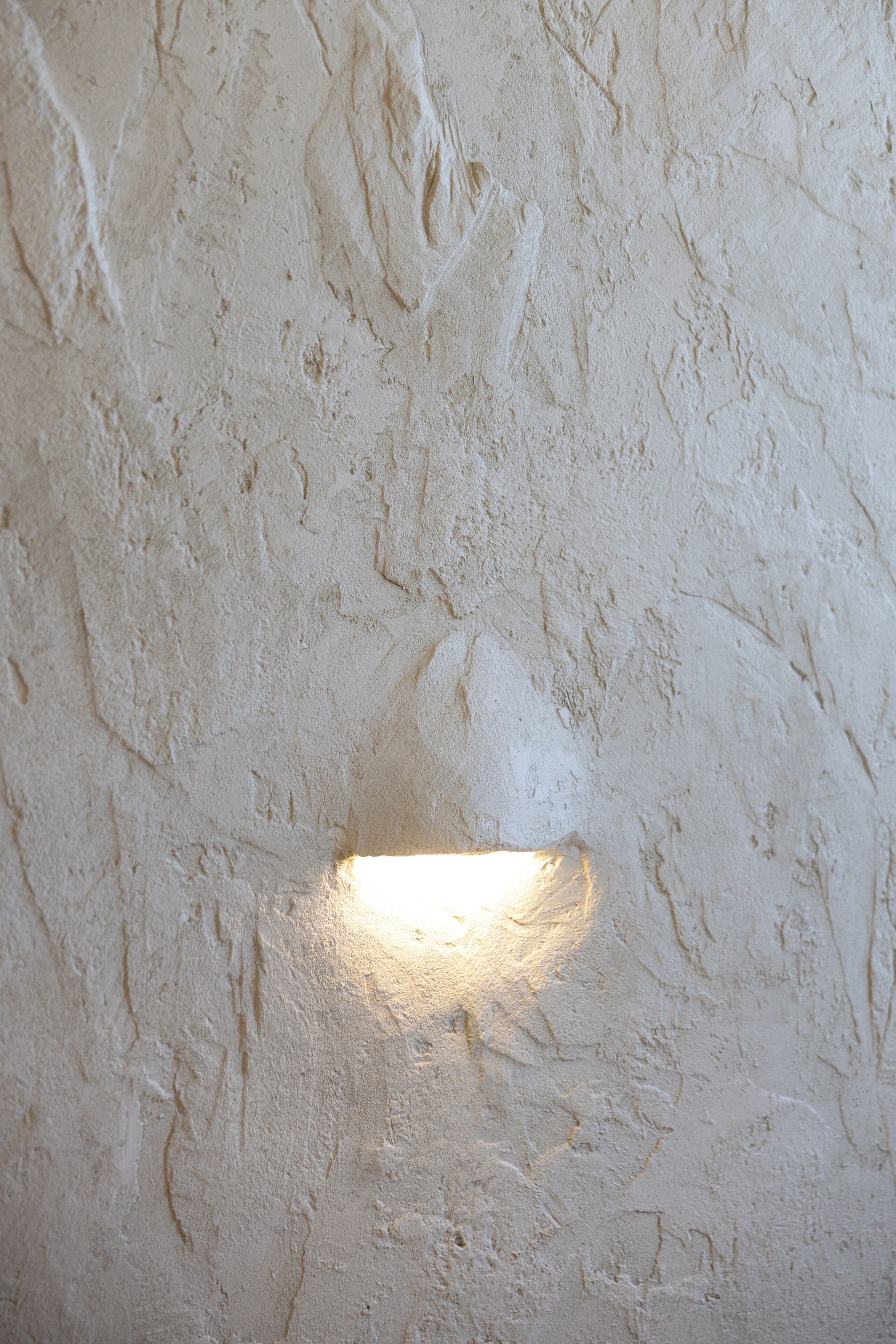 A textured wall with a small, illuminated window.