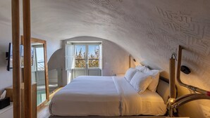 A bedroom with a bed, a window, and a ceiling with etched designs. - Santorini Soul Villas (Santorini)