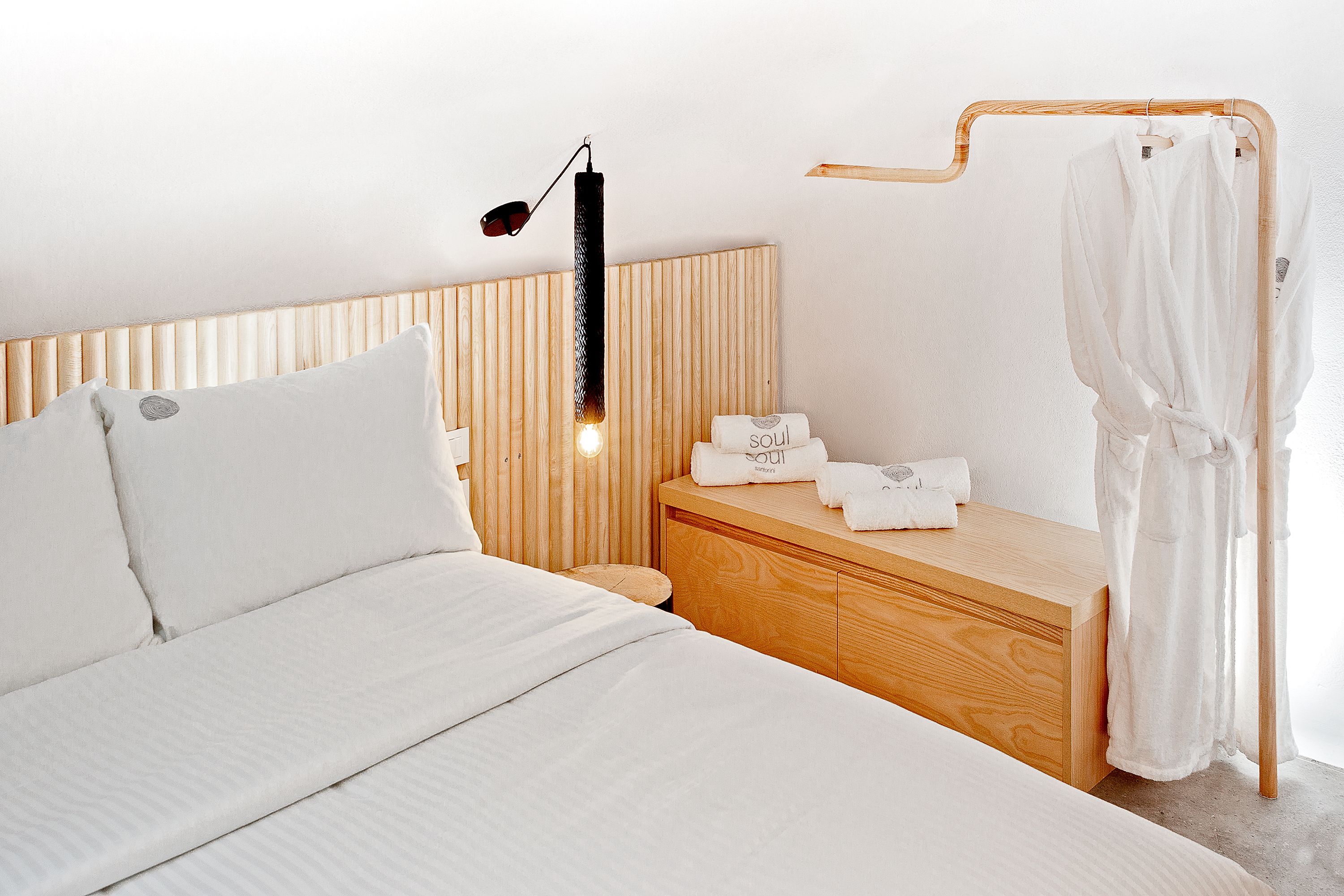 Un dormitorio moderno con cabecera de madera, una mesita de noche con toallas y un perchero.