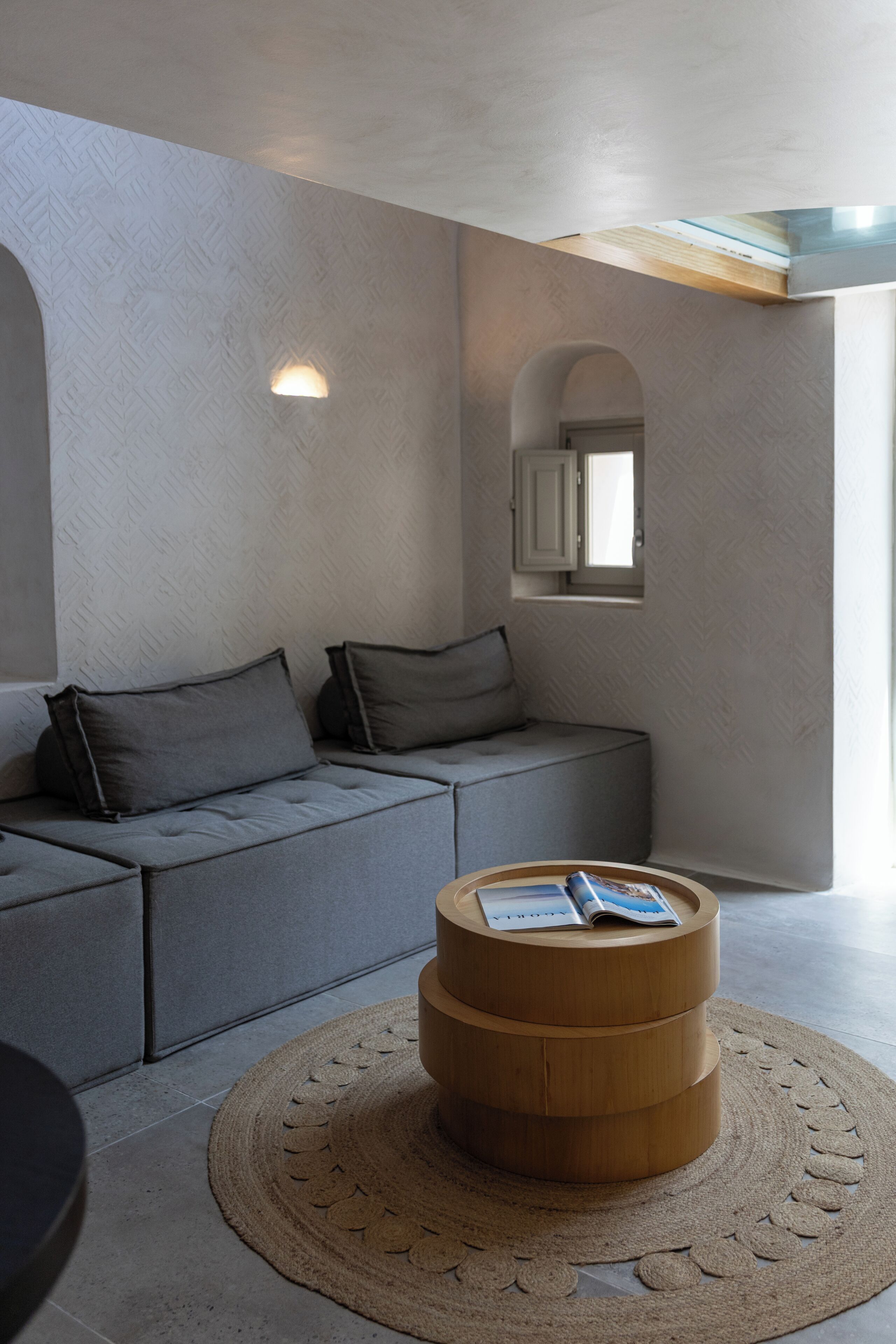 A modern room with a grey sofa, a wooden coffee table with magazines, and a patterned rug.