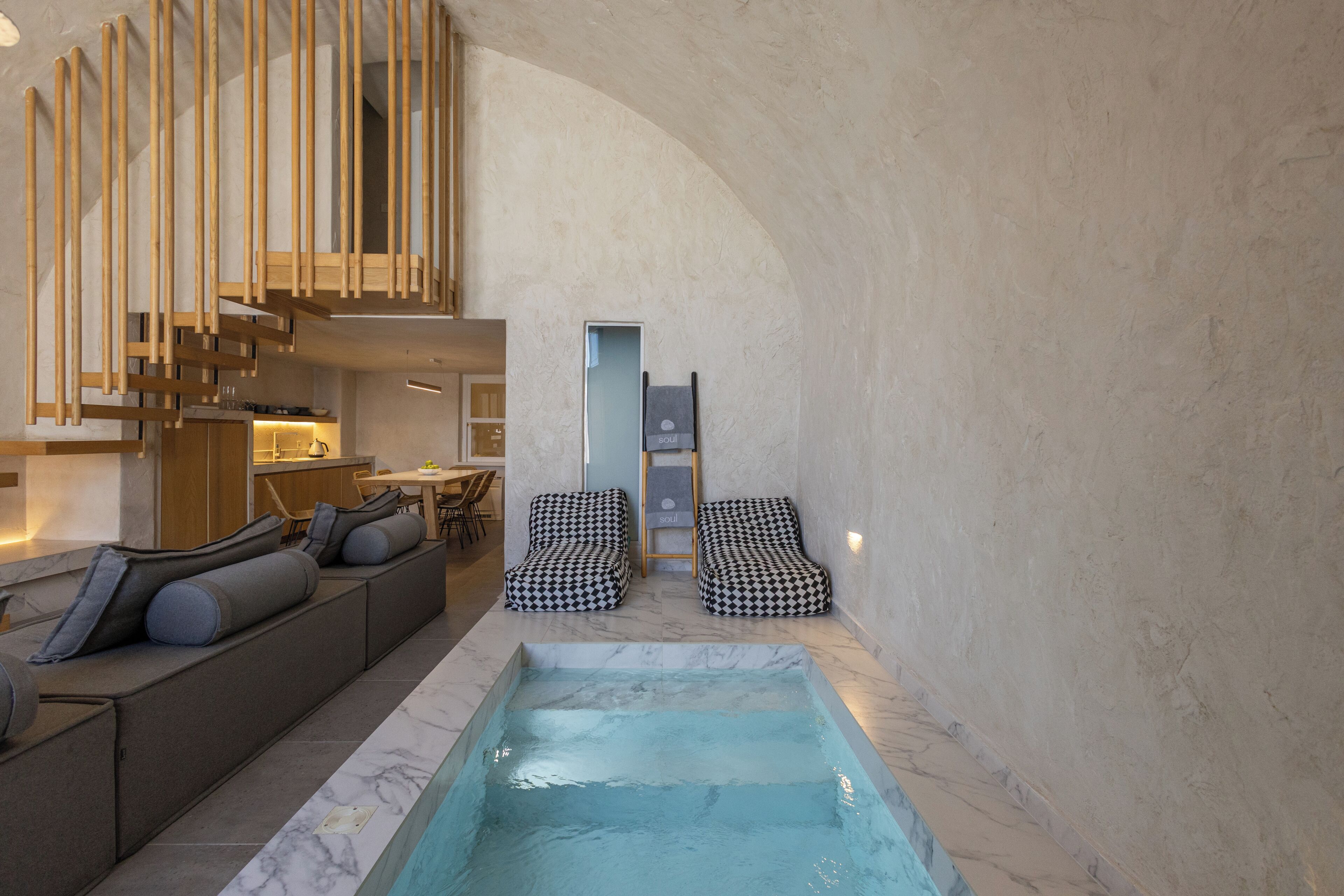 A modern interior with a pool, seating area, and a staircase.