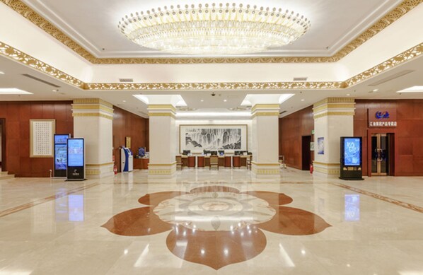 A spacious lobby with a central chandelier, a reception desk, and digital information kiosks.