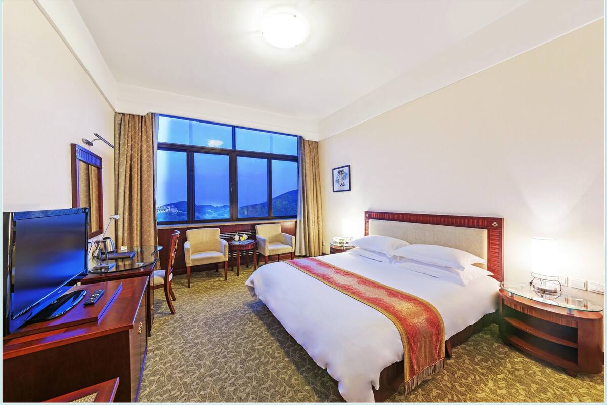 Een hotelkamer met een groot bed, een bureau met een computer, een televisie en een raam met gordijnen.