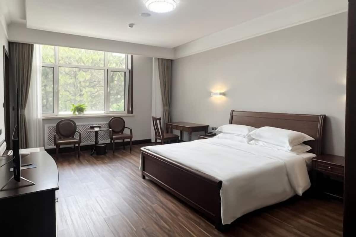 Een hotelkamer met een groot bed, een bureau met stoel, een kleine tafel en een raam met gordijnen.