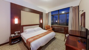 A hotel room with a large bed, a desk with a TV, a chair, a nightstand with a phone, and a window with curtains. - Dalian Bangchui Island Hotel (Dalian)