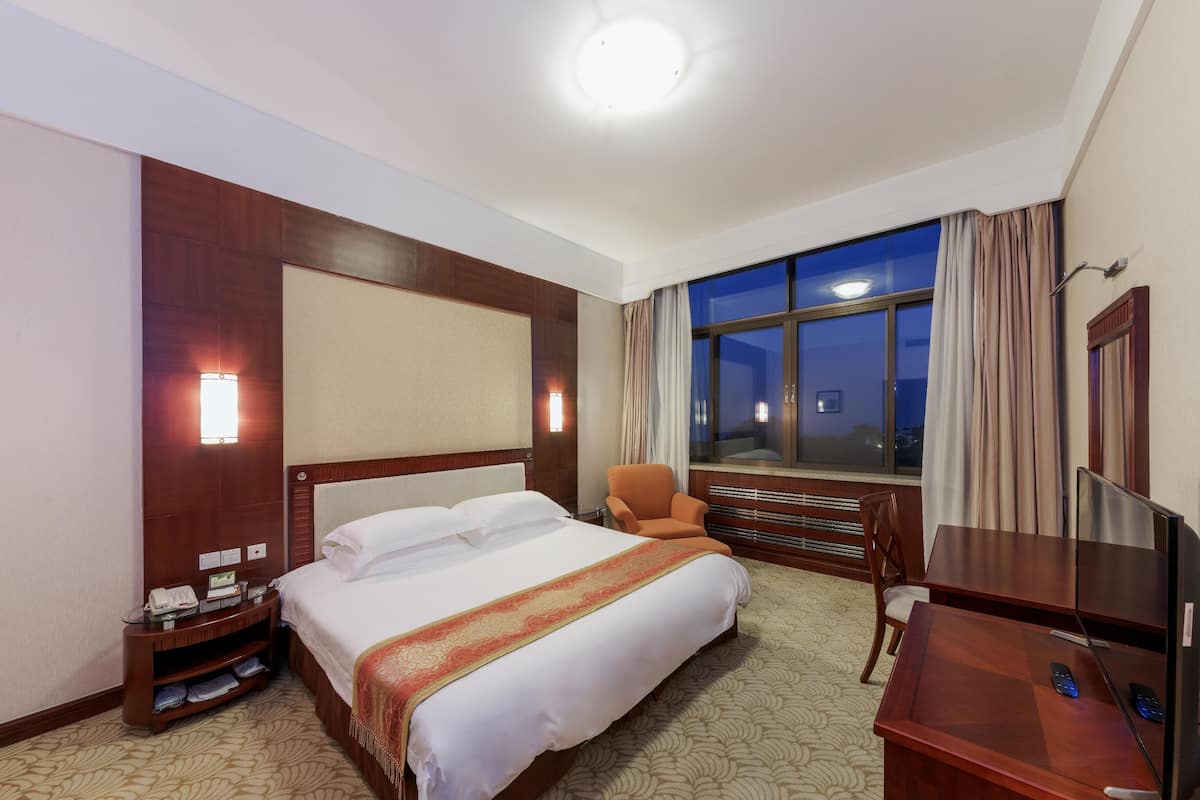Een hotelkamer met een groot bed, een bureau met een televisie, een stoel, een nachtkastje met een telefoon en een raam met gordijnen.