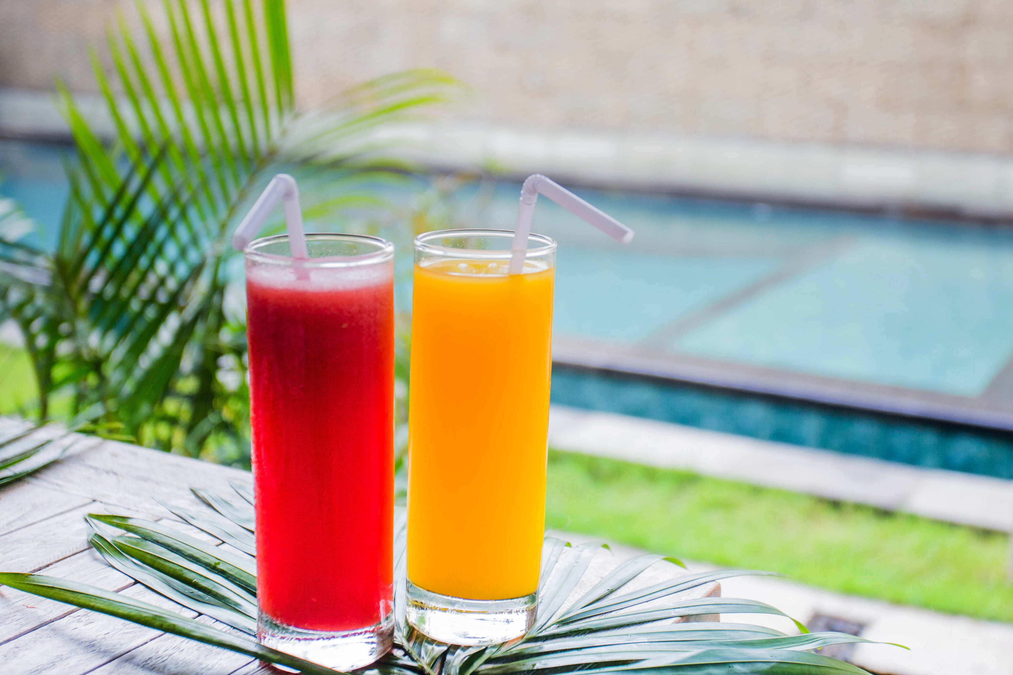 Two drinks on a table with a pool in the background.